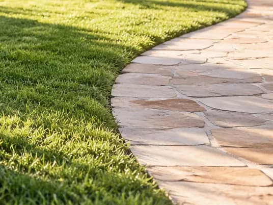 A clean sandstone path curving beside a green lawn.